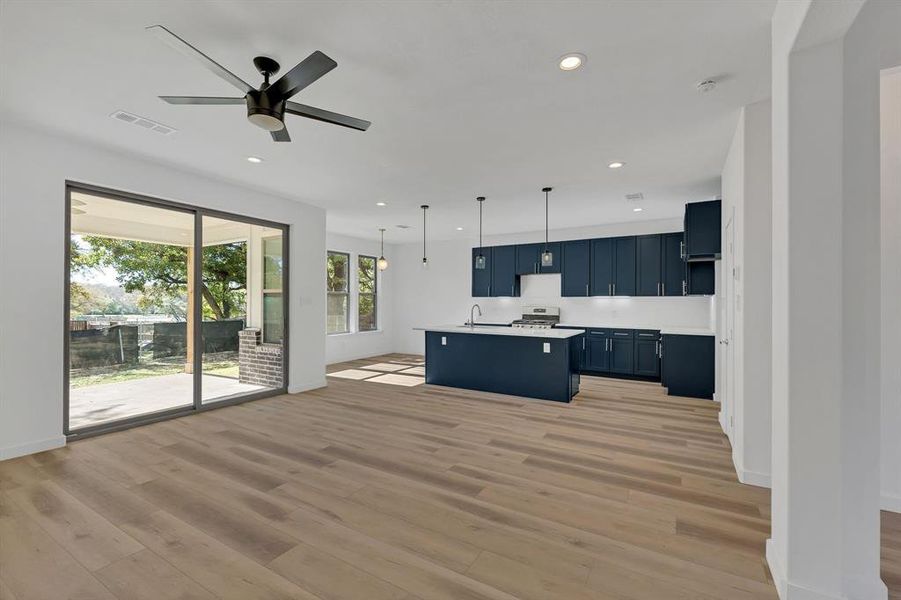 Kitchen featuring light countertops, decorative light fixtures, an island with sink, open floor plan, and light wood-style floors