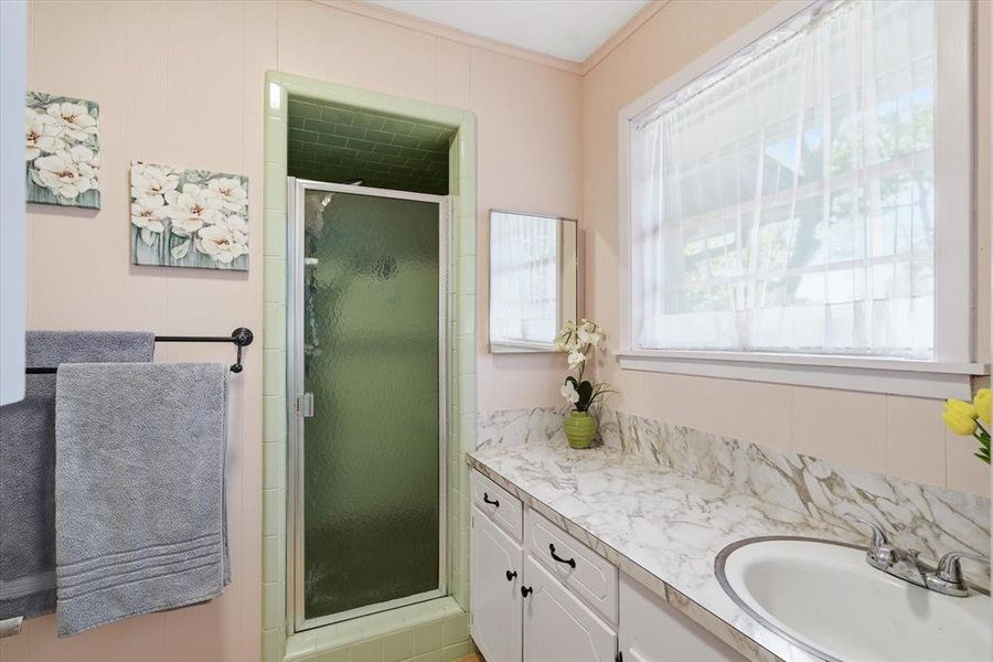 Bathroom featuring a walk-in shower with green tiled walls and a glass door, a vanity with white cabinetry, a white basin sink, and a patterned countertop