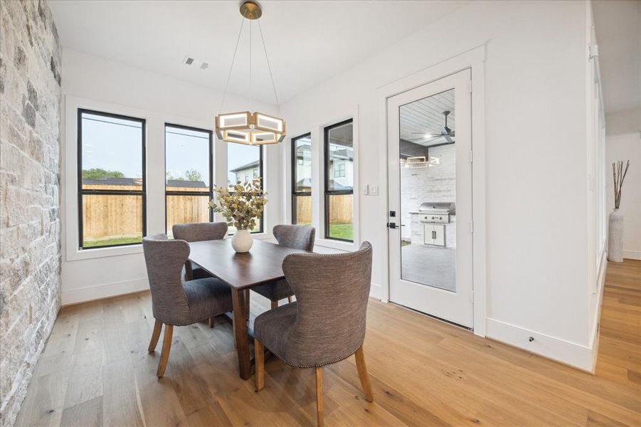 The breakfast area stands out with a stone accent wall, transitional chandelier, plenty of windows and a door to the outdoor kitchen.