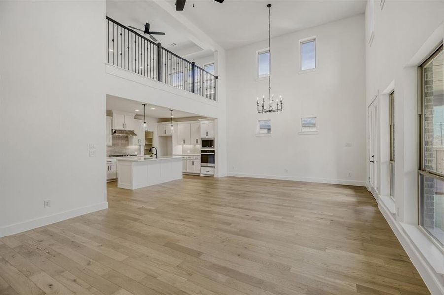 Unfurnished living room with a ceiling fan, a chandelier, light wood finished floors, and a high ceiling