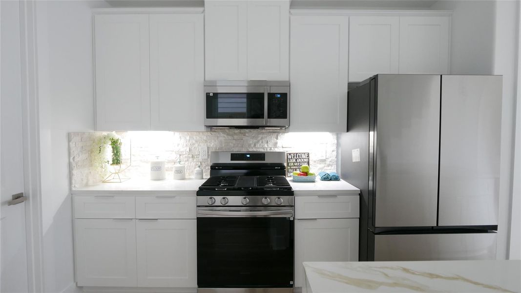This kitchen features modern stainless steel appliances, including a gas stove and a double-door refrigerator. It has sleek white cabinetry, a stylish backsplash, and under-cabinet lighting, creating a bright and contemporary space. This kitchen features modern stainless steel appliances, including a gas stove and a double-door refrigerator. It has sleek white cabinetry, a stylish backsplash, and under-cabinet lighting, creating a bright and contemporary space.