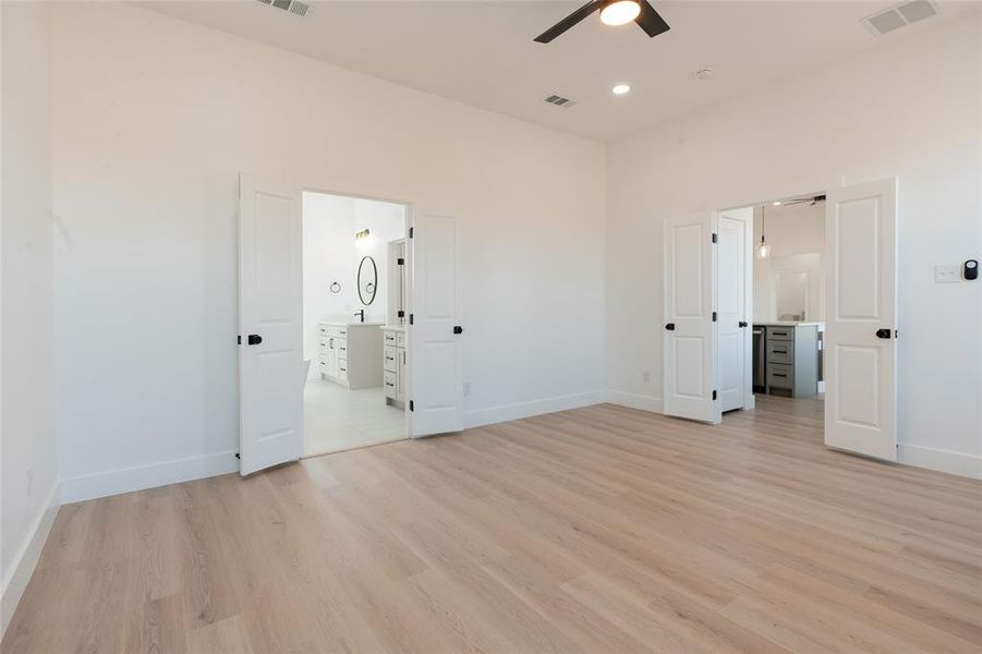 Spacious primary bedroom featuring an ensuite bathroom, light wood-style flooring, ceiling fan, and recessed lighting