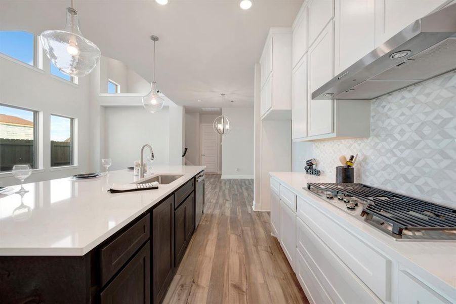 Kitchen with two tone color scheme, range hood, stainless steel appliances, light wood-type flooring, and light stone countertops