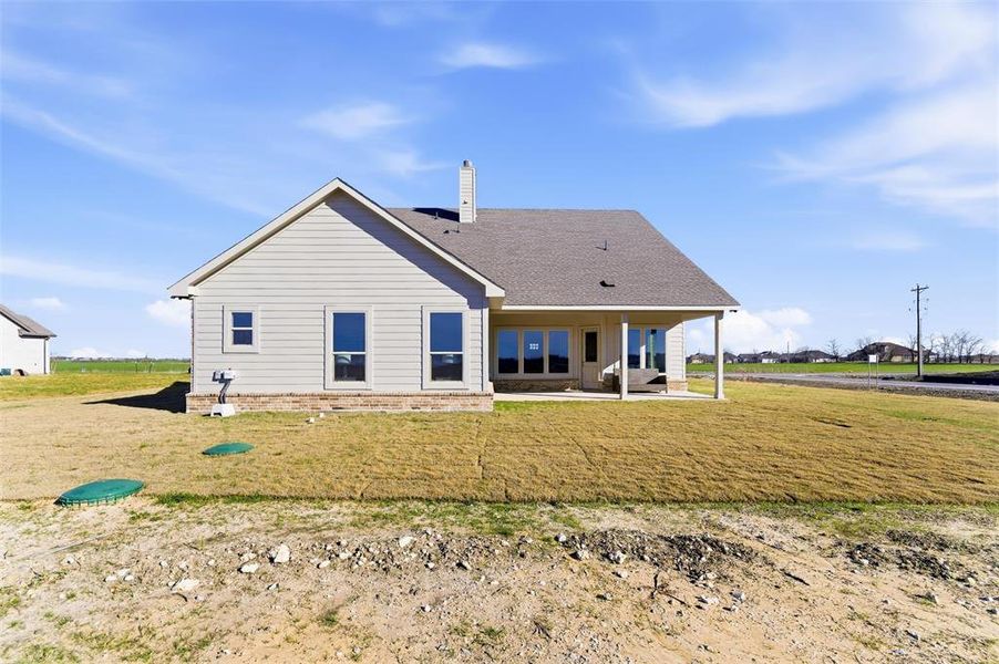 Back of property with a chimney, a patio, a lawn, and a shingled roof