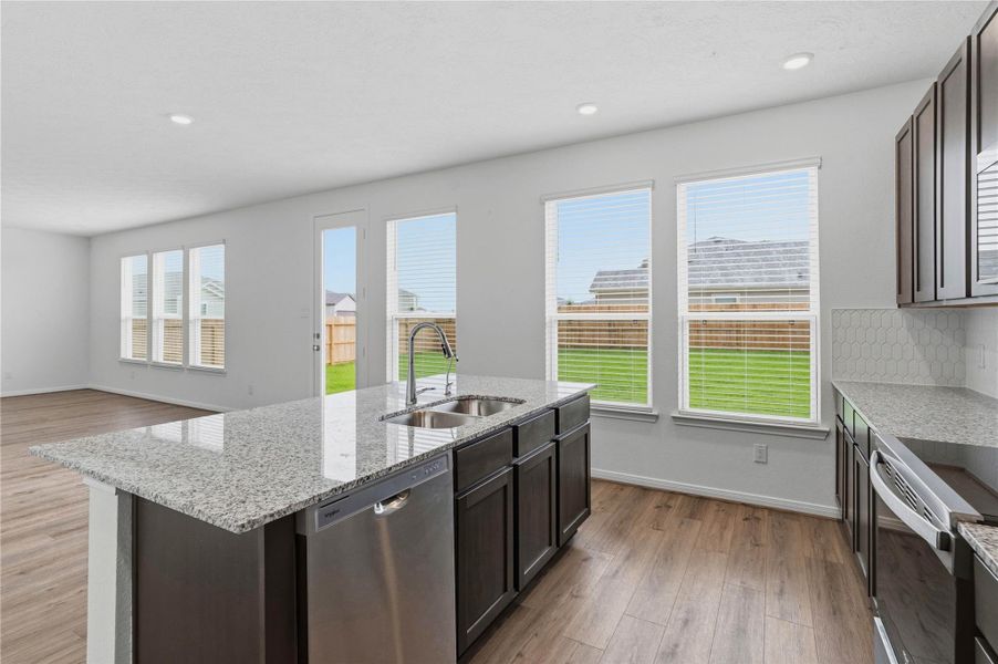 This kitchen boasts high ceilings, Woodmont Dakota cabinets in Smoke stain, Luna Pearl Granite countertops, stainless steel Whirlpool appliances, a modern Daltile backsplash, recessed lighting, an added breakfast bar to kitchen countertop, and a pantry—all overlooking the expansive Great Room.