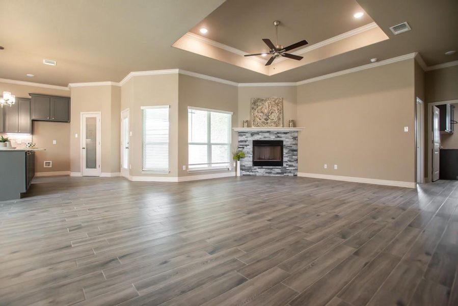 Unfurnished living room featuring ceiling fan, wood finished floors, a tray ceiling, a fireplace, and crown molding Unfurnished living room featuring ceiling fan, wood finished floors, a tray ceiling, a fireplace, and crown molding
