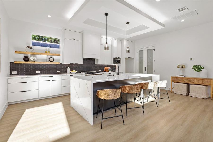 Kitchen featuring light wood-type flooring, backsplash, an island with sink, white cabinets, and custom exhaust hood