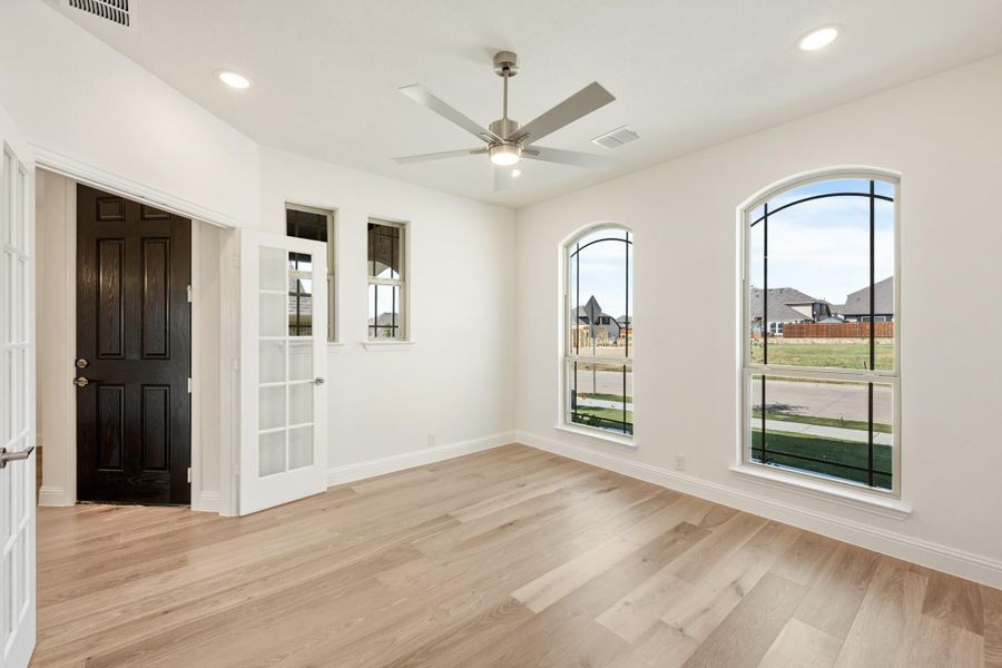 Empty room with light wood floors, ceiling fan, arched windows, and a dark wood front door nearby. Empty room with light wood floors, ceiling fan, arched windows, and a dark wood front door nearby.