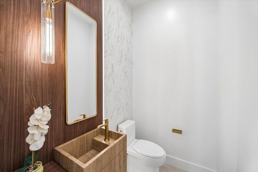 Elegant powder room featuring a custom made Travertine sink, accented by a modern gold-framed mirror and stylish lighting. Elegant powder room featuring a custom made Travertine sink, accented by a modern gold-framed mirror and stylish lighting.