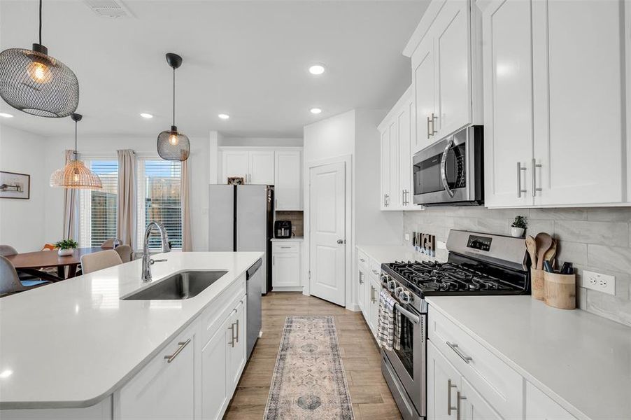 Kitchen featuring appliances with stainless steel finishes, pendant lighting, white cabinetry, sink, and a kitchen island with sink