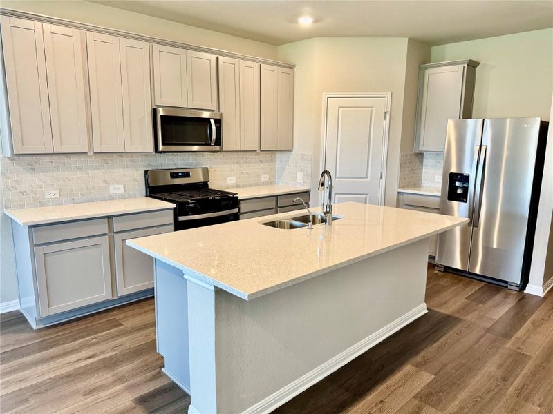 Kitchen with appliances with stainless steel finishes, tasteful backsplash, wood finished floors, light stone counters, and recessed lighting Kitchen with appliances with stainless steel finishes, tasteful backsplash, wood finished floors, light stone counters, and recessed lighting