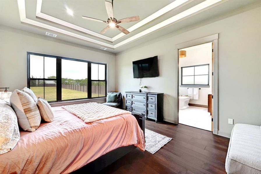 Bedroom featuring a raised ceiling, dark wood-style floors, a ceiling fan, and connected bathroom