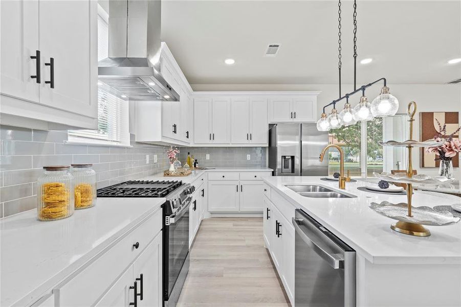 Kitchen featuring stainless steel appliances, pendant lighting, tasteful backsplash, white cabinets, and light stone countertops Kitchen featuring stainless steel appliances, pendant lighting, tasteful backsplash, white cabinets, and light stone countertops