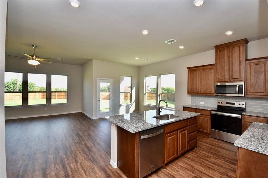 Kitchen featuring brown cabinets, stainless steel appliances, recessed lighting, light stone counters, and dark wood-style flooring