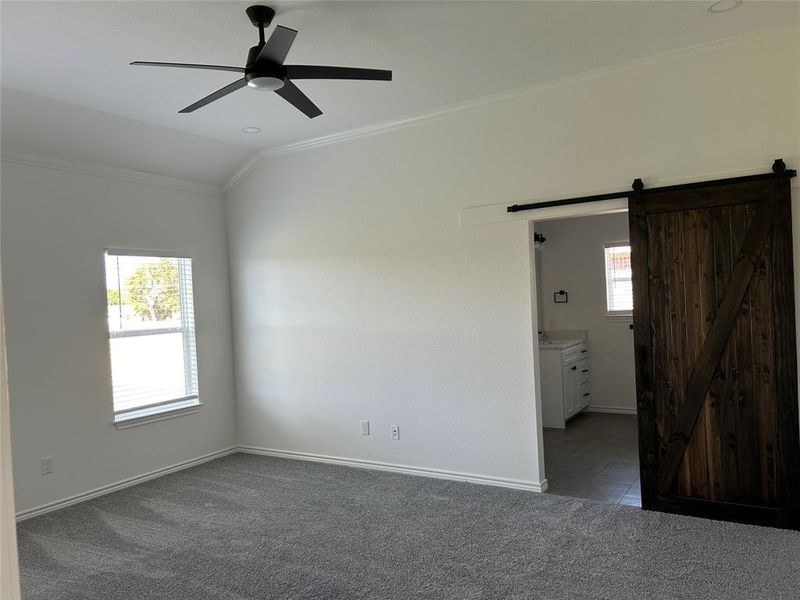 Unfurnished bedroom with crown molding, dark colored carpet, ceiling fan, ensuite bath, and a barn door