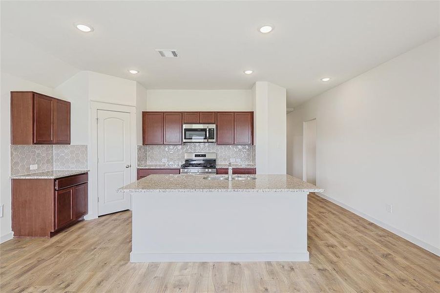 Kitchen with light stone counters, a center island with sink, light wood-type flooring, and appliances with stainless steel finishes