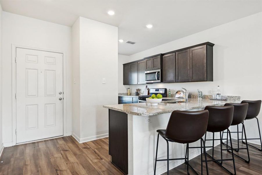 Kitchen with kitchen peninsula, light stone countertops, a kitchen bar, black range with gas cooktop, and hardwood / wood-style floors