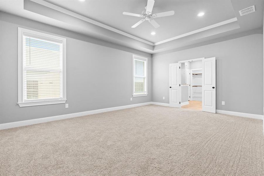 Primary bedroom with ensuite bathroom, visible vents, light carpet, a raised ceiling, and baseboards Primary bedroom with ensuite bathroom, visible vents, light carpet, a raised ceiling, and baseboards