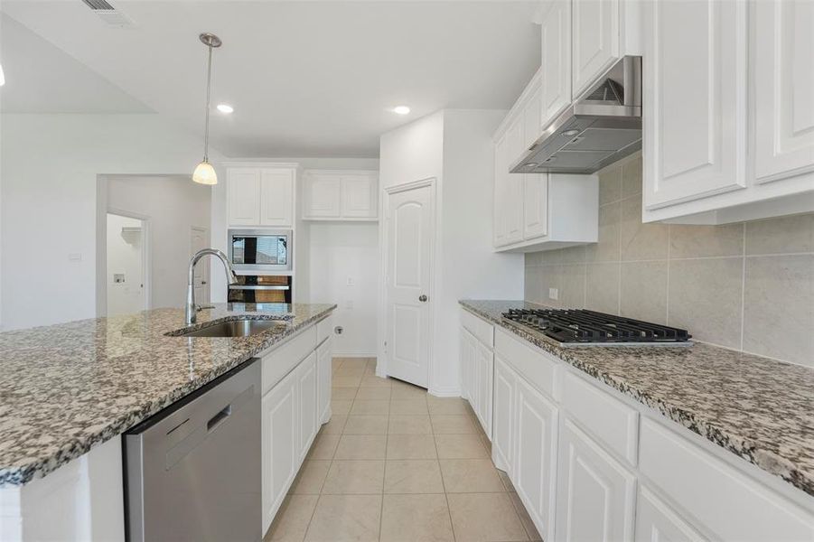 Kitchen with sink, light stone countertops, hanging light fixtures, appliances with stainless steel finishes, and white cabinetry