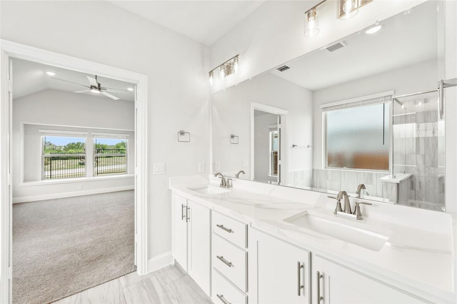 Ensuite bathroom with double vanity, white cabinets, quartz countertops, and view into carpeted bedroom. Ensuite bathroom with double vanity, white cabinets, quartz countertops, and view into carpeted bedroom.