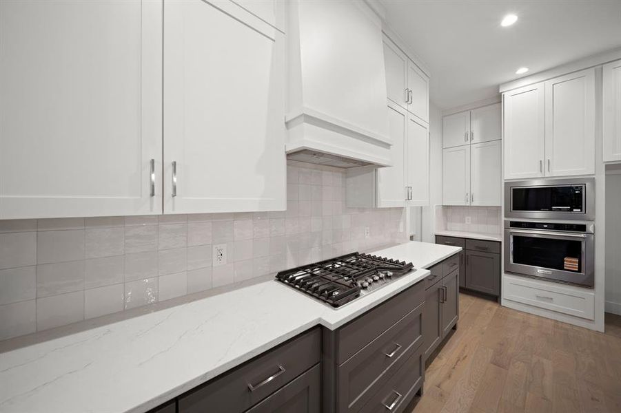 Kitchen featuring white cabinets, tasteful backsplash, stainless steel appliances, custom exhaust hood, and recessed lighting