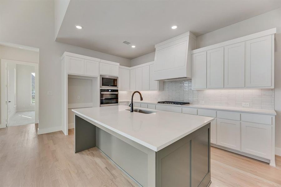 Kitchen with white cabinetry, backsplash, light wood-style floors, a kitchen island with sink, and recessed lighting Kitchen with white cabinetry, backsplash, light wood-style floors, a kitchen island with sink, and recessed lighting