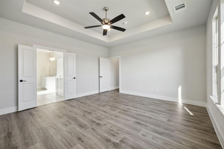 Unfurnished bedroom featuring ceiling fan, a raised ceiling, light wood-type flooring, and connected bathroom