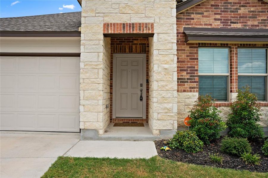 View of exterior entry featuring stone siding, brick siding, a shingled roof, and an attached garage