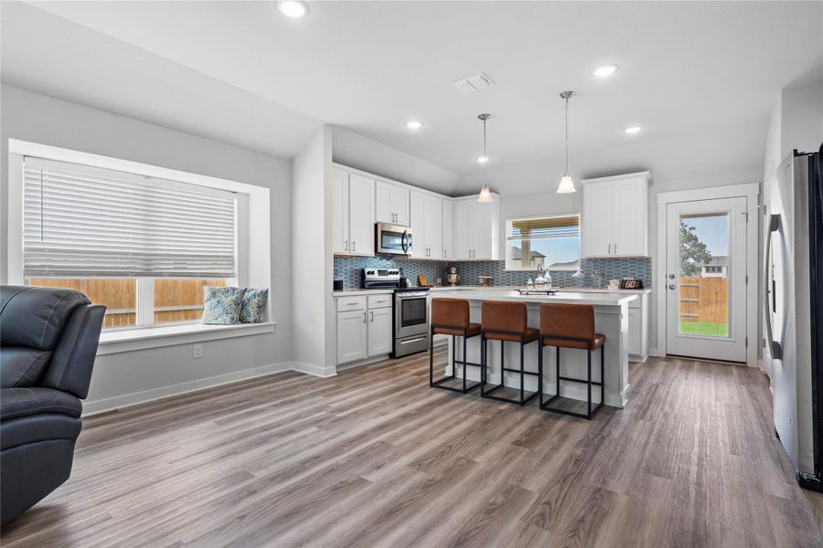 Kitchen featuring appliances with stainless steel finishes, open floor plan, a kitchen bar, light countertops, and white cabinetry Kitchen featuring appliances with stainless steel finishes, open floor plan, a kitchen bar, light countertops, and white cabinetry