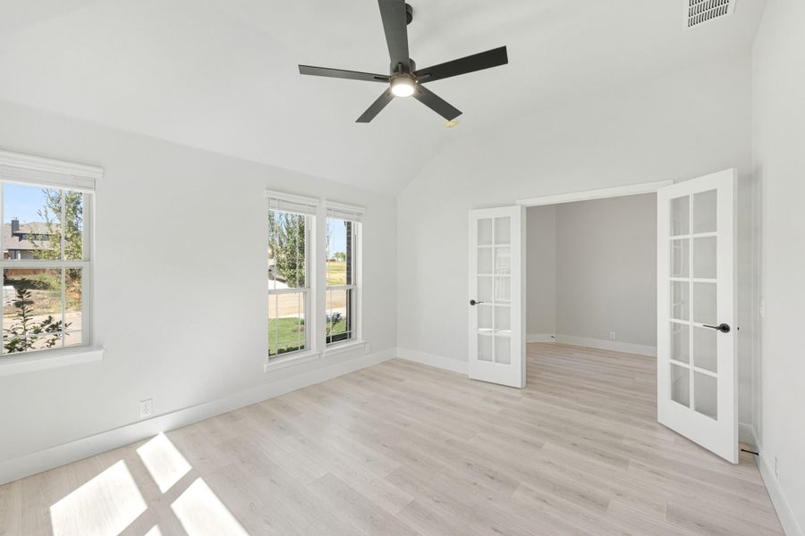Empty bedroom with vaulted ceiling, ceiling fan, light wood floors, and French doors leading to a closet or sitting room