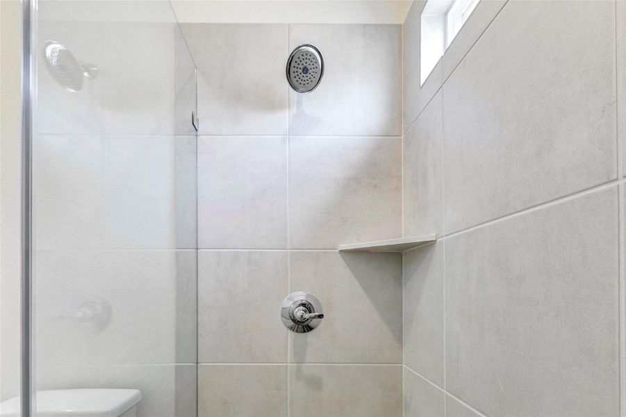 A closer look at the walk-in shower showcases neutral tile surround, chrome shower fixtures, a built-in corner shelf, and a high window that brings in natural light while maintaining privacy. The clean design and simple finishes create a fresh, functional bathroom detail. A closer look at the walk-in shower showcases neutral tile surround, chrome shower fixtures, a built-in corner shelf, and a high window that brings in natural light while maintaining privacy. The clean design and simple finishes create a fresh, functional bathroom detail.