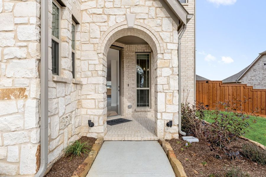 Stone home entrance with arched doorway, brick walkway, and landscaped front yard