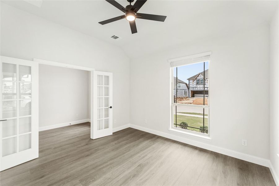 Empty room with hardwood floors, ceiling fan, and French doors leading to adjacent space Empty room with hardwood floors, ceiling fan, and French doors leading to adjacent space