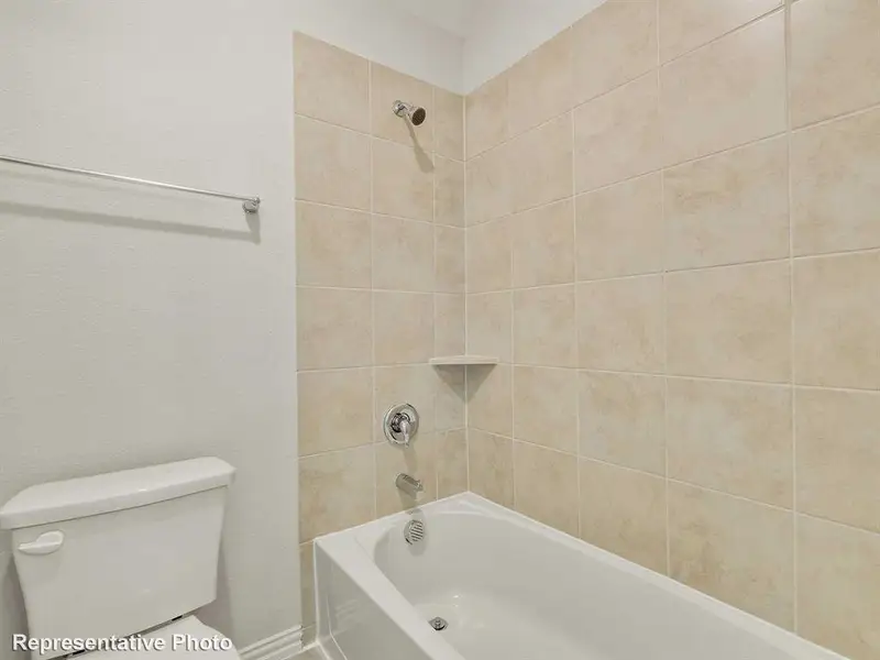 Bathroom featuring a white bathtub, a tiled shower surround with a built-in shelf, and a white toilet