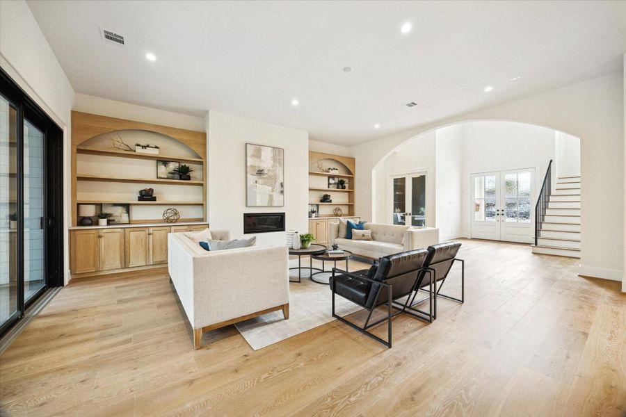 Open living room with custom onsite built-ins, sleek fireplace, white oak wood floors, and arched entry to the foyer.