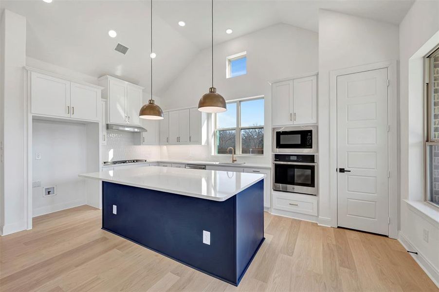 Dual tone kitchen featuring stainless steel oven, a center island, lofted ceiling, pendant lighting, and built in microwave Dual tone kitchen featuring stainless steel oven, a center island, lofted ceiling, pendant lighting, and built in microwave