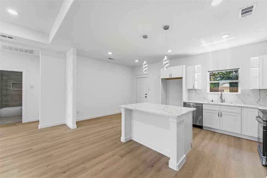 Contemporary kitchen featuring a central island with a stone-finish countertop, white cabinetry, stainless steel dishwasher, and designer pendant lighting