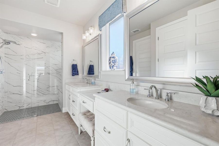 Full bath featuring two vanities, a marble finish shower, and light tile patterned floors