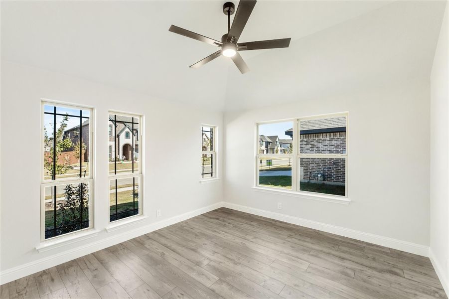Empty room with vaulted ceiling, ceiling fan, hardwood floors, and multiple windows with neighborhood views