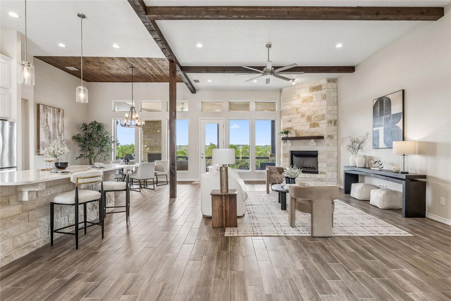 A spacious great room features rich exposed beams, a stone-clad fireplace, and expansive windows offering serene outdoor views.