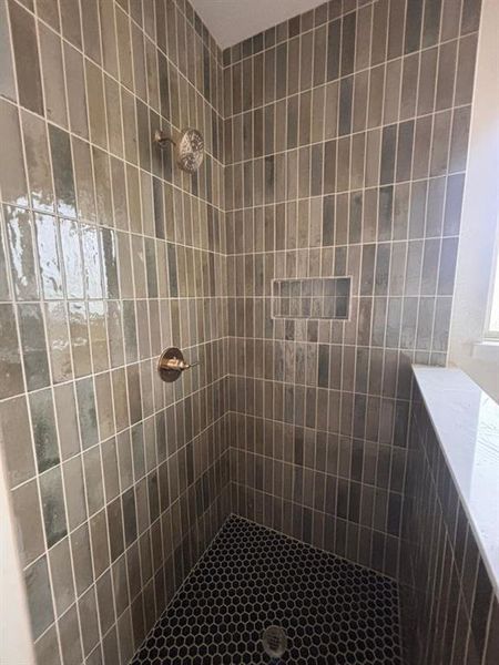Tiled shower with vertical subway tile walls, a built-in shower niche, and a contrasting hexagonal mosaic floor