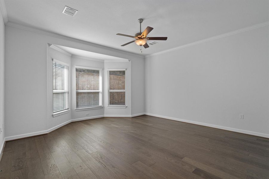 Empty room with ceiling fan, ornamental molding, and dark wood finished floors Empty room with ceiling fan, ornamental molding, and dark wood finished floors