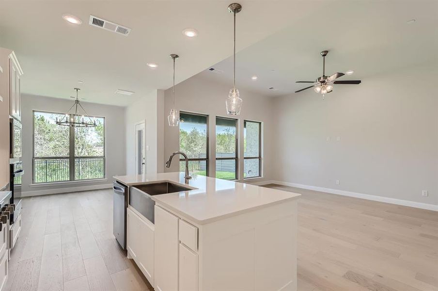 Kitchen with decorative light fixtures, ceiling fan with notable chandelier, light wood-type flooring, and a kitchen island with sink