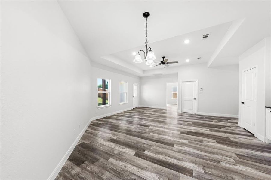 Empty room featuring a tray ceiling, wood finished floors, a chandelier, and recessed lighting Empty room featuring a tray ceiling, wood finished floors, a chandelier, and recessed lighting