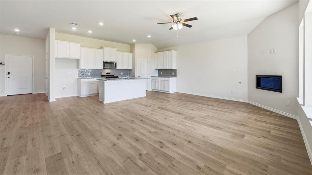 Kitchen with open floor plan, white cabinets, light wood-style flooring, decorative backsplash, and stainless steel appliances