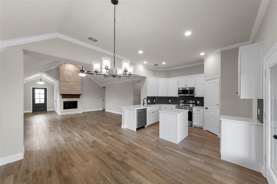 Expansive open concept living area featuring wood-finish flooring, a stone fireplace with a wood mantel, and vaulted ceilings