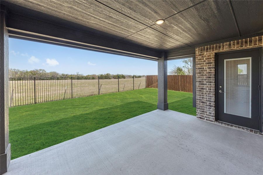 Covered concrete patio with green backyard, metal fence, and brick exterior wall with back door