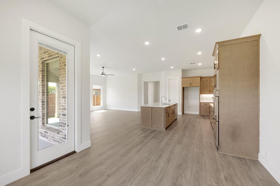 Open-concept living area with kitchen island, wood cabinets, light hardwood floors, and glass back door
