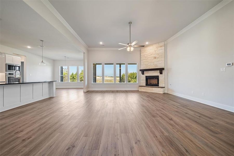 Unfurnished living room with crown molding, healthy amount of natural light, a fireplace, dark wood finished floors, and a ceiling fan Unfurnished living room with crown molding, healthy amount of natural light, a fireplace, dark wood finished floors, and a ceiling fan