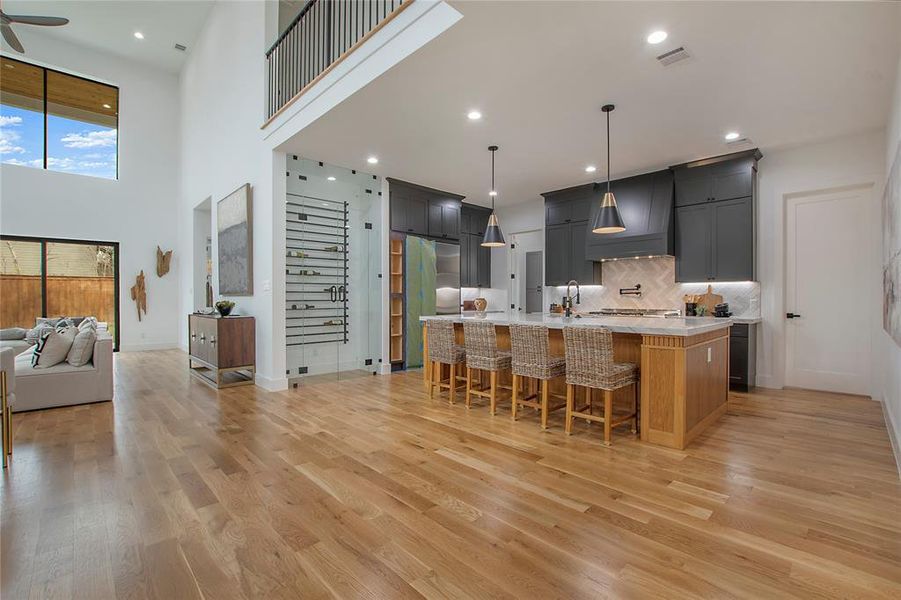 Kitchen featuring a kitchen island with sink, hanging light fixtures, custom range hood, and light hardwood / wood-style floors